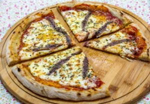 Wood-fired Italian pizza topped with melted mozzarella, tomato sauce, and anchovies, sliced and served on a wooden board.