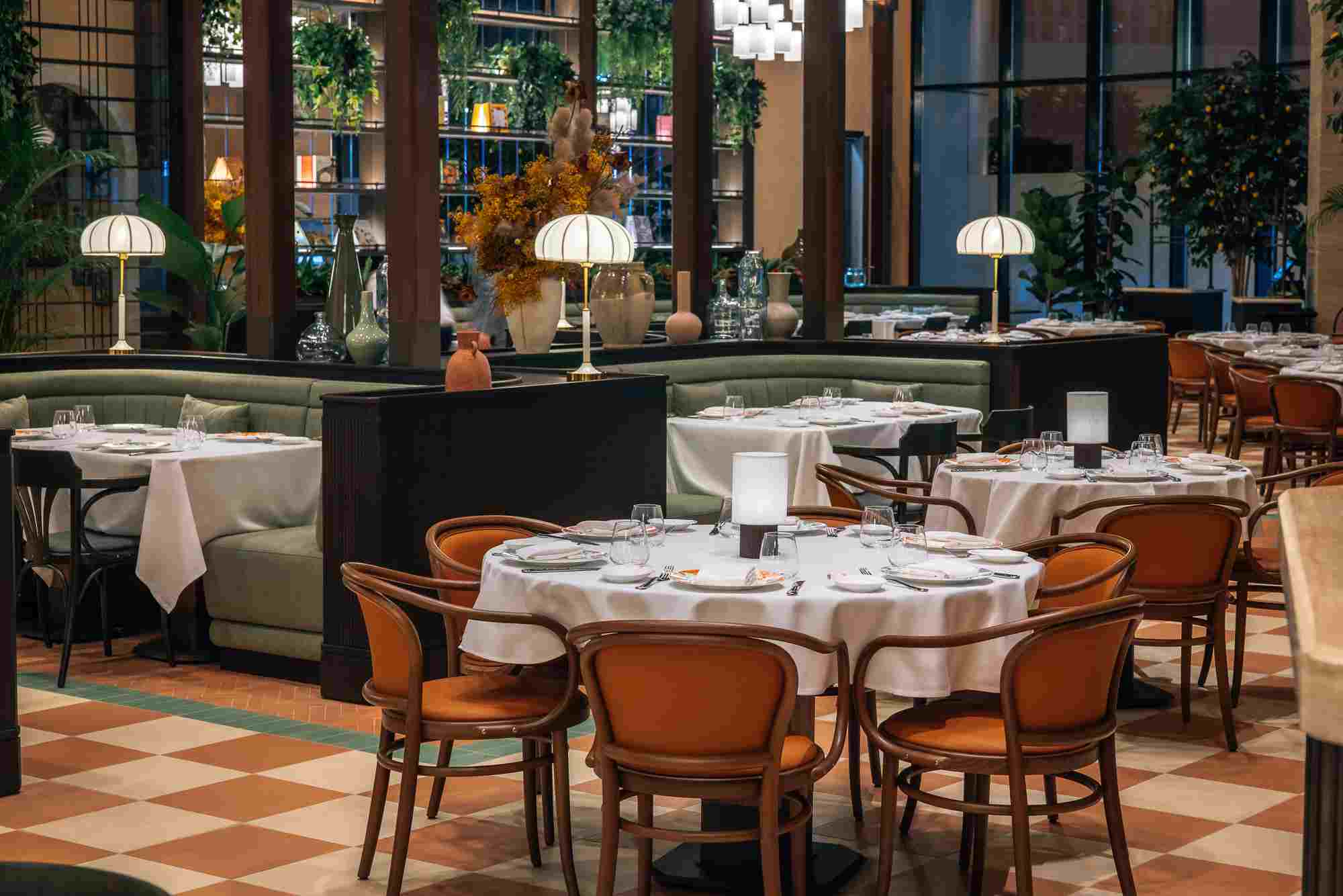 Indoor Dining Close-up of a table in an Italian restaurant with wooden chairs and greenery in the background