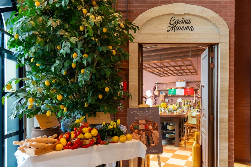 Italian restaurant entrance with lemon tree, rustic decor, fresh vegetables display, and open kitchen view creating a warm and authentic dining atmosphere