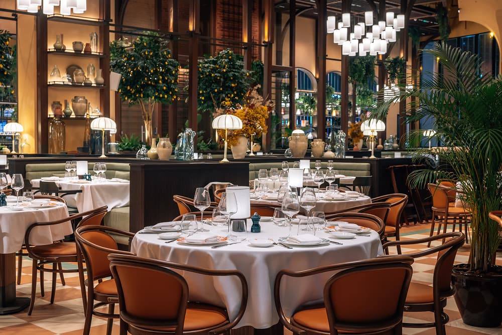 Mamabella restaurant interior with elegant dining tables, warm lighting and lush greenery.