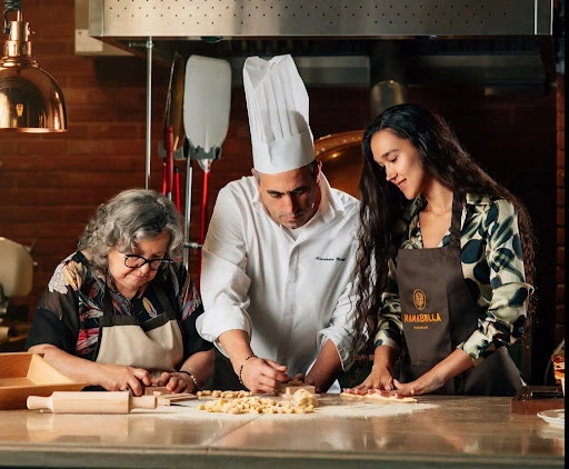 A visiting nonna, Chef Alessandro Miceli, and a guest shape pasta by hand at the open kitchen counter at Mamabella